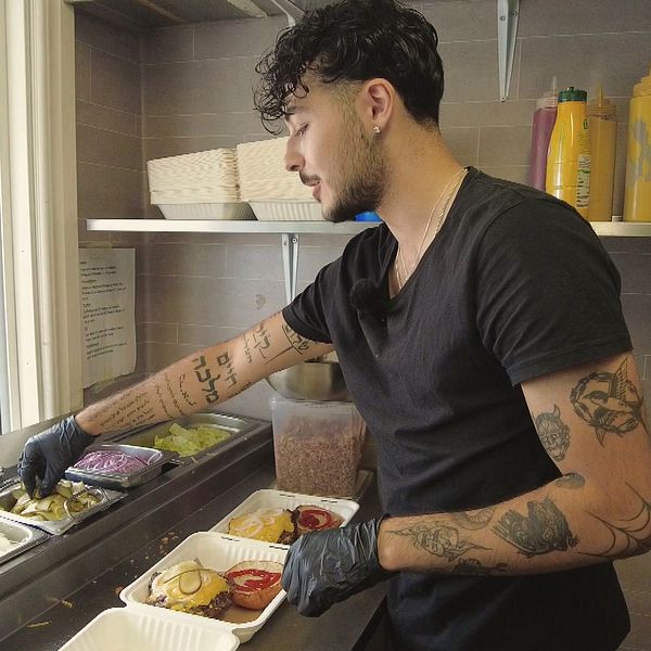 Daniel i sin restaurangvagn i Umeå när han fyller matlådor med hamburgare.
