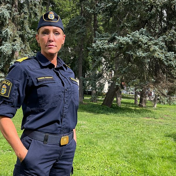 En kvinnlig polis som ser allvarlig ut i en solig park med träd i bakgrunden