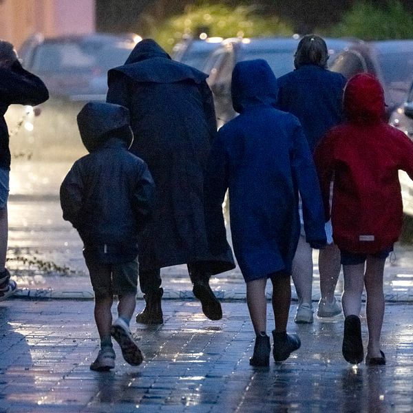 Folk i regnkläder på trottoar i blåst och regn.