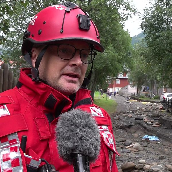 Räddningsledare Karl Groves på plats vid Susabäcken i Åre, med röda räddningskläder. Bakom honom syns förödelsen på platsen.