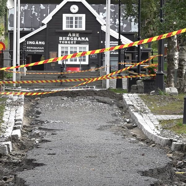 Huset där det står Åre Bergbana torget är i bakgrunden, och framför den är en trasig asfaltväg avtejpad med varningstejp.