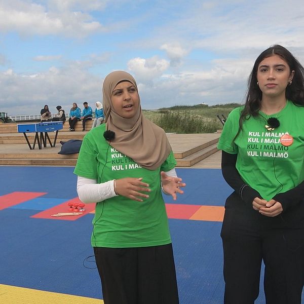 Två tjejer i gröna t-shirts som står vid en strand.