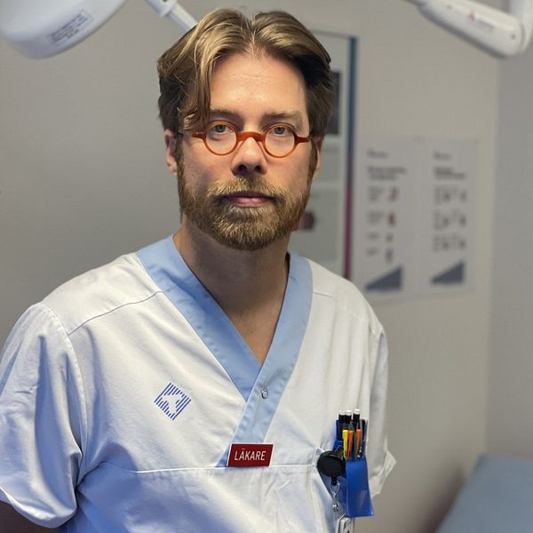Läkaren Jonas Stenberg står i ett sjukhusrum i vita sjukhuskläder.