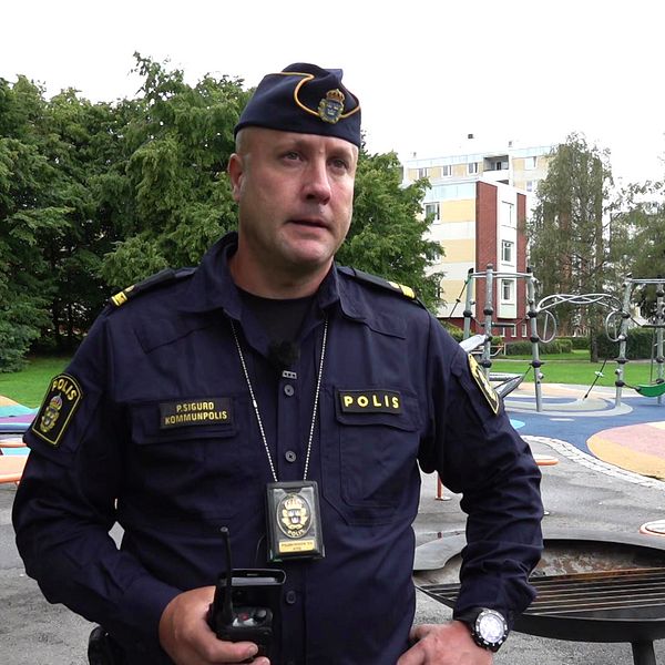 En manlig polis i uniform står på en lekplats i Årby i Eskilstuna där en mamma och flicka besköts för ett år sedan.