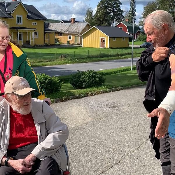 En man i rullstol och en kvinna som knuffar på tittar på en annan man som visar upp sina skador efter att ha blivit attackerad av en björn.