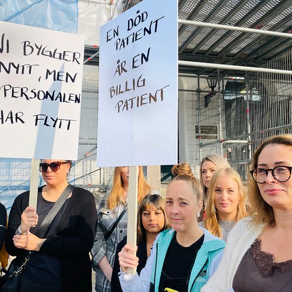 Läkare, sjuksköterskor och undersköterskormed plakat med texten ”Ni bygger nytt, men personalen har flytt” och ”En död patient är en billig patient”.