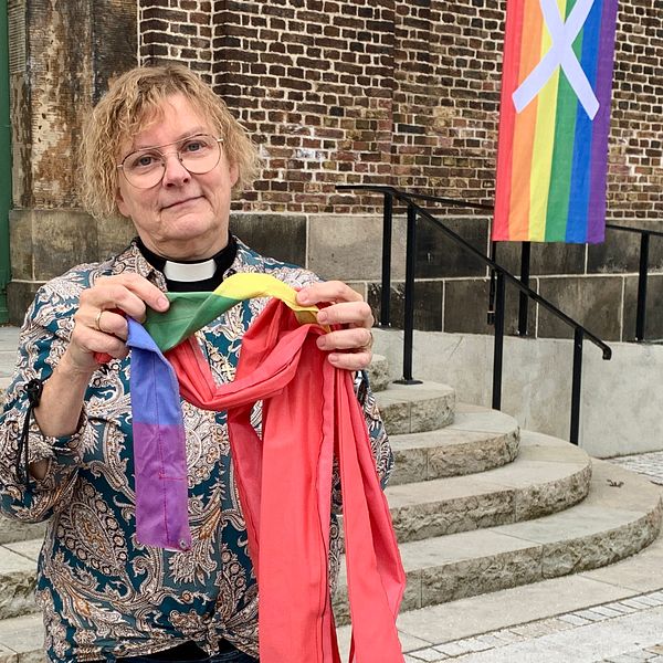 Kyrkoherden Eva-Lotta Grantén håller upp en del av en bränd regnbågsflagga utanför Sofia Albertina kyrkan.