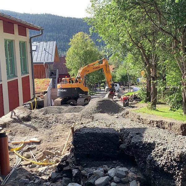 Bild från Åre by som drabbades av stora översvämningar under ovädret Hans. Ett hus som till synes hänger i luften och en grävmaskin som fyller i de djupa eroderingarna.