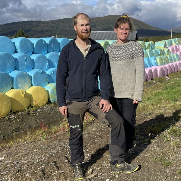 En man och en kvinna står framför högar av höbalar.