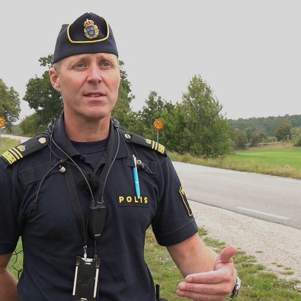 Manlig polis i uniform och med polismössa står intill en 70-väg och tittar snett till höger i bild. Petter Wahllöf, trafikpolis, Karlskrona. Silletorpsvägen, Allatorp, Rosenholm.
