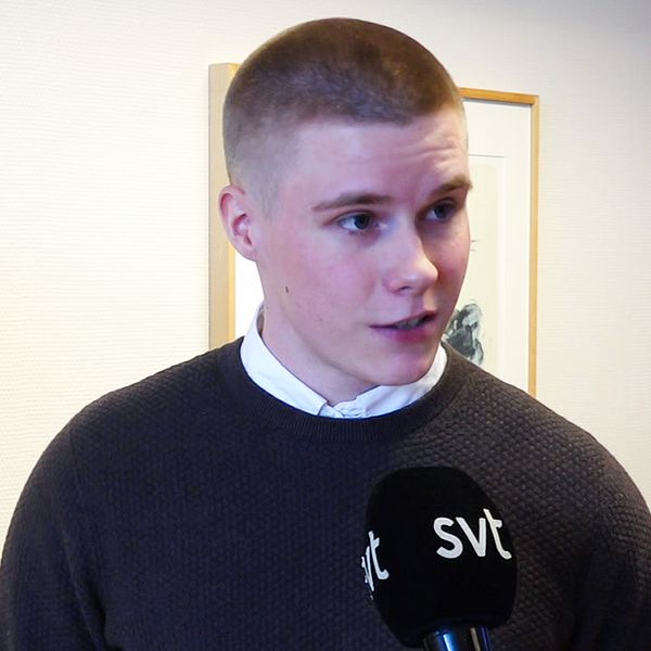 en korthårigman står i en brun tröja framför en vit vägg.