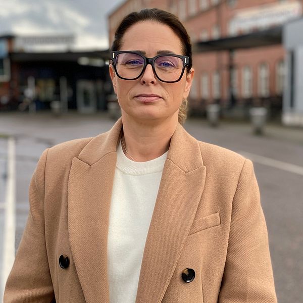 Lisa Bertilsson i glasögon och beige kappa framför akutmottagningen i Lidköping