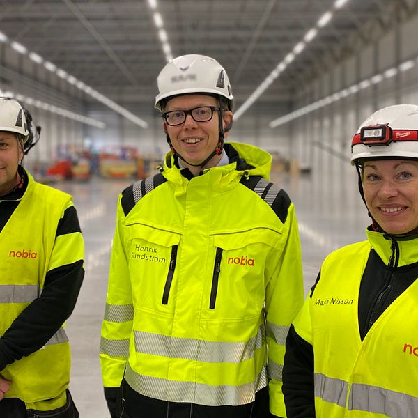 Tre personer i varselväst ler i Nobias nya fabrikslokaler på Torsvik i Jönköping.