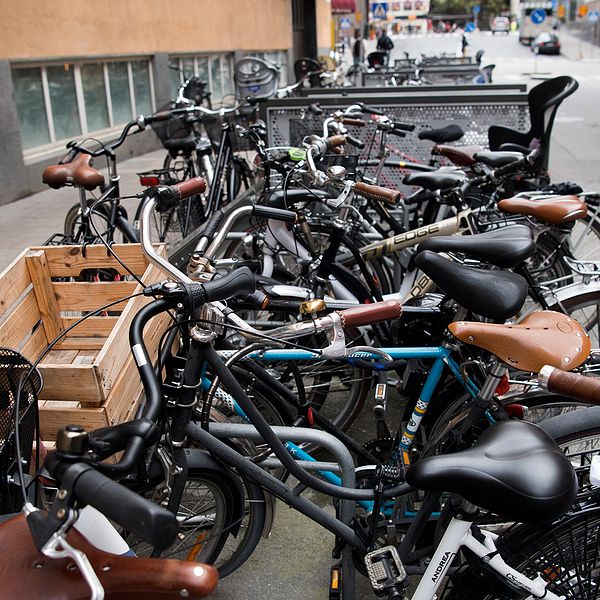 Flertalet cyklar står uppställda vid en trottoar.