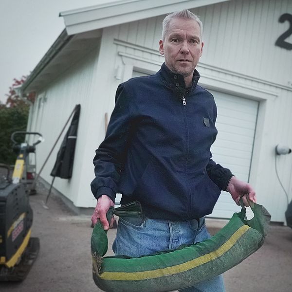 En man står på en garageuppfart med en sandsäck i famnen.