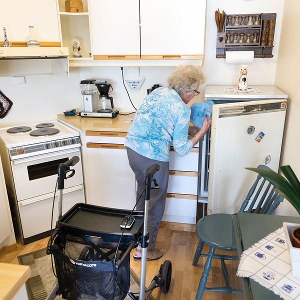 Äldre kvinna öppnar kylskåp.