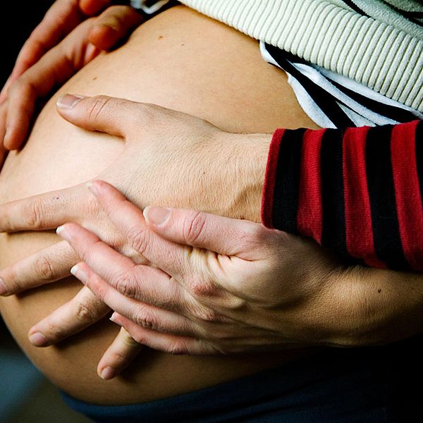 Gravid kvinna med händer på sin mage.