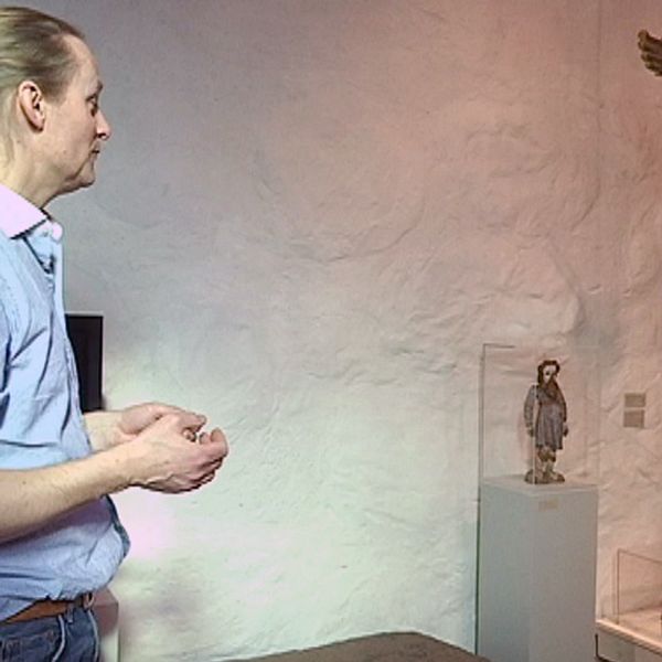 Man med blå skjorta och hästsvans står framför konstverk på en vit vägg på ett museum