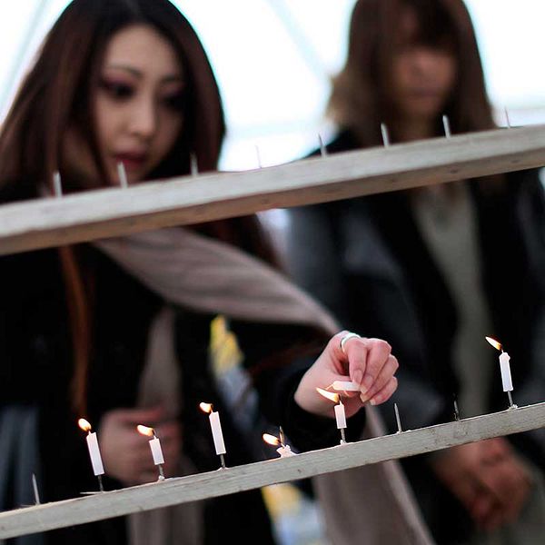 Ung kvinna tänder ljus för offren på femårsdagen av Fukushima-katastrofen.