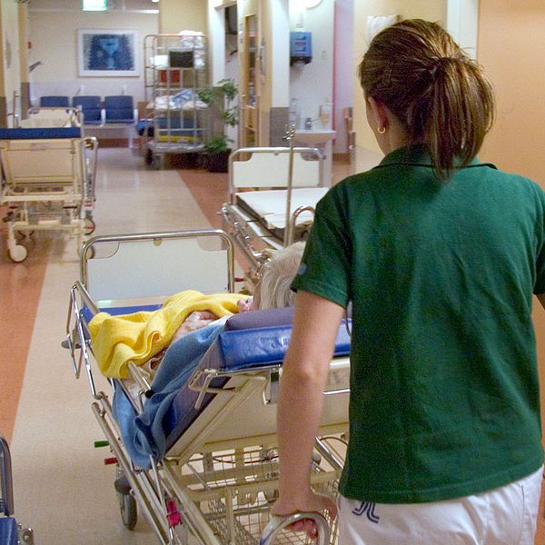 Sjukvårdspersonal flyttar patient i sjukhussäng i korridor.