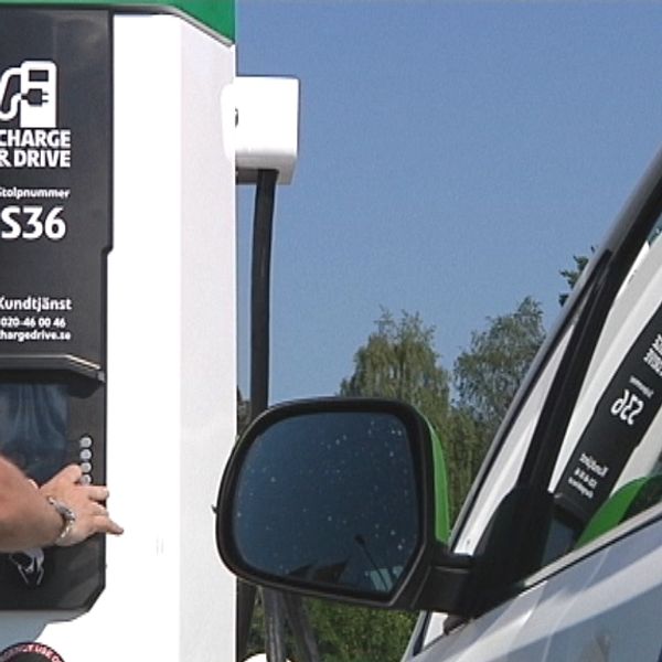 En bil står intill en laddstation. En man trycker på en av knapparna på laddstationen.