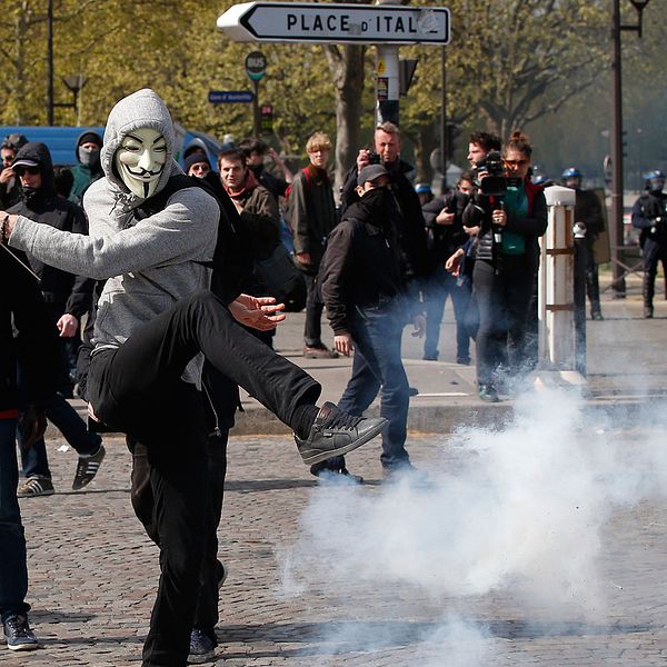 En maskerad demonstrant sparkar till en tårgasbehållare.
