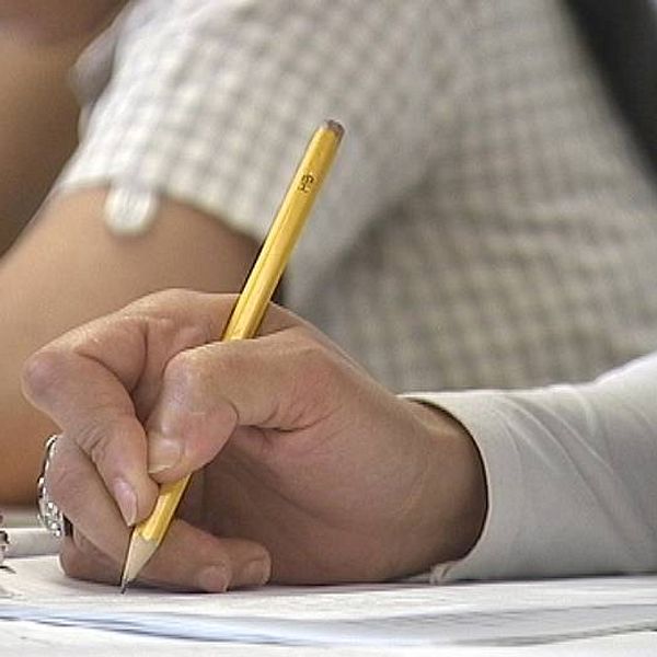 Tät bild på students hand skrivande med blyertspenna.