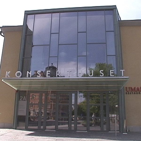 Entrén till Konserthuset med stora glasfönster och skylten ”KONSERTHUSET” i fronten, omgiven av grönska och stadsbyggnader i bakgrunden.