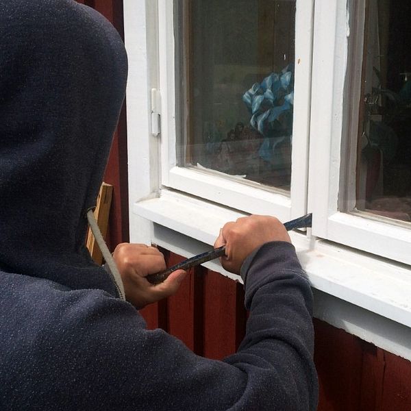 Anonym inbrottstjuv med huvtröja som har en kofot vid ett villafönster