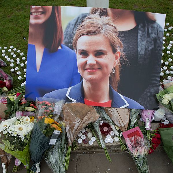 Porträttbild på Jo Cox omringad av blommor och ljus vid en minnesplats.