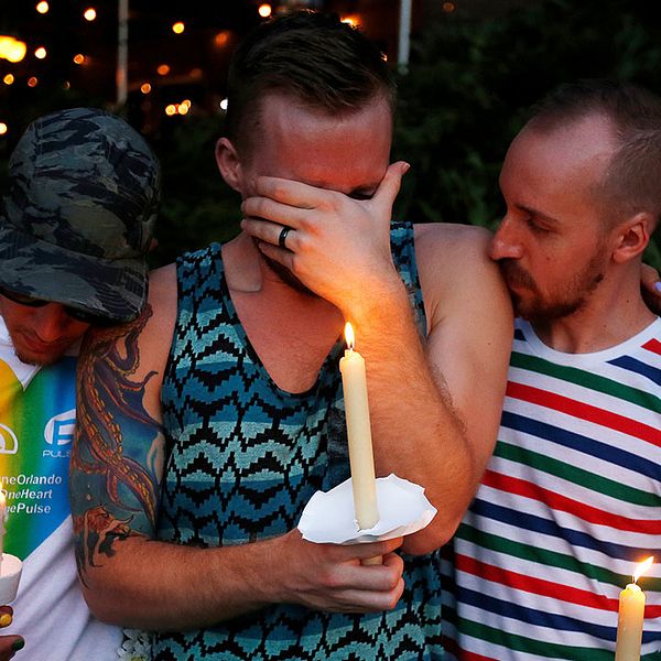 Tre män som deltar i ljusvakan i Orlando gråter tillsammans.