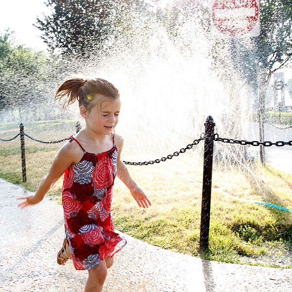 Flicka springer förbi en vattenspridare