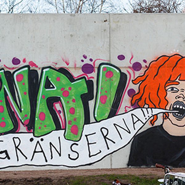 Halmstadkonstnären Minna Svensson intill det verk hon gjorde på Halmstadväggen i samband med väggens öppnande hösten 2015. Verket är ett självporträtt och i kombination med graffitin intill lyder texten ”Öppna gränserna”.