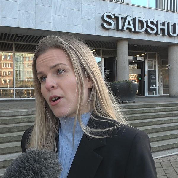 Person framför stadshuset intervjuas av media utanför byggnaden.