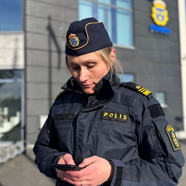 Polis i uniform utanför polisstationen med sin mobiltelefon.