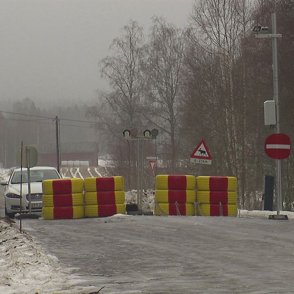 Avspärrad väg med bommar och skyltar i vintermiljö. En bil närmar sig bommarna.