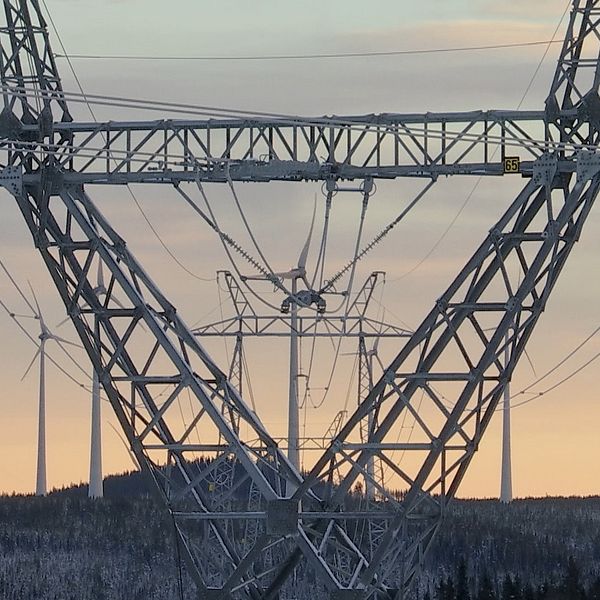 kraftledningsstolpe med vindkraftsverk i bakgrunden