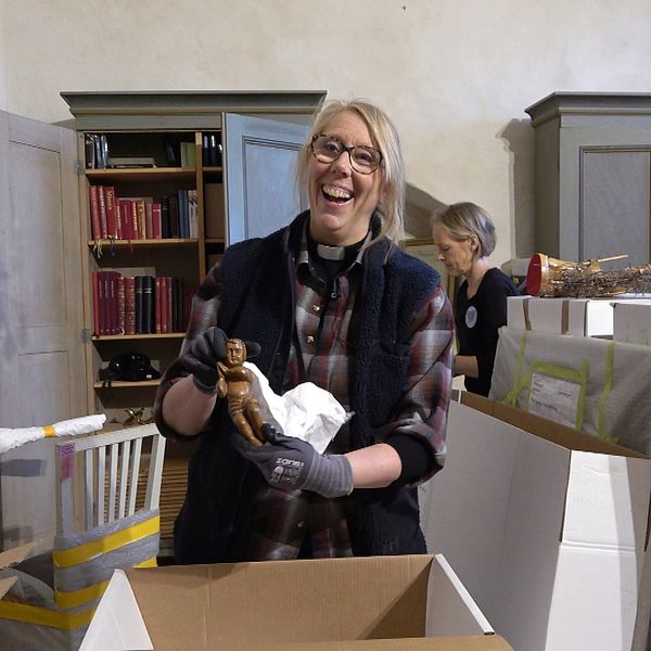 Kyrkoherden Beatrice Lönnqvist packar upp föremål ur en låda i ett rum med bokhyllor och skåp i Botkyrka kyrka.