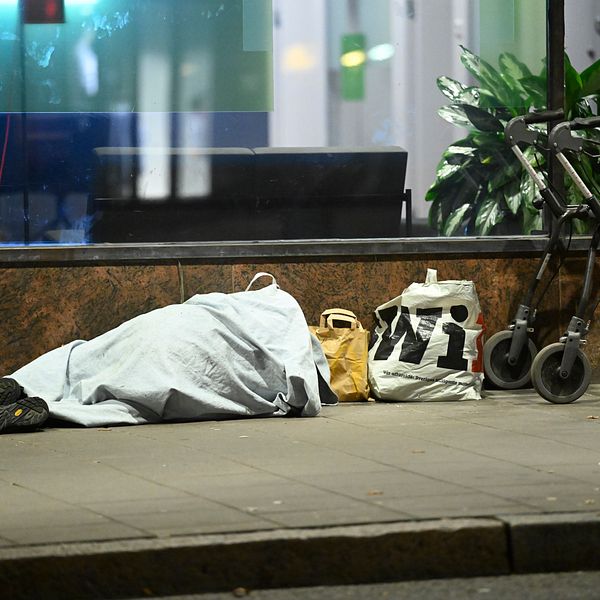 En hemlös ligger på marken utanför en byggnad.
