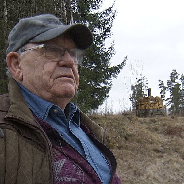 Mannens kropp framför en skog med ett grävmaskin i bakgrunden. Skogsskylt syns.