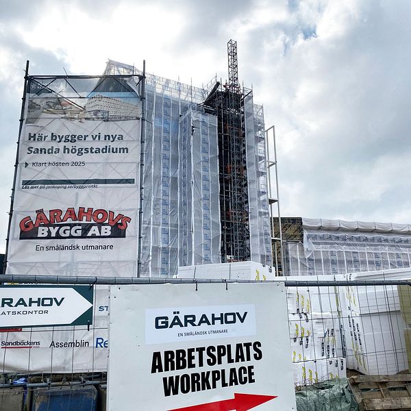 Byggarbetsplats för nya Sanda högstadium under uppförande. Byggnaden är täckt med byggställningar och presenningar. Skyltar från entreprenören Garahov Bygg AB finns på stängslet framför byggarbetsplatsen.