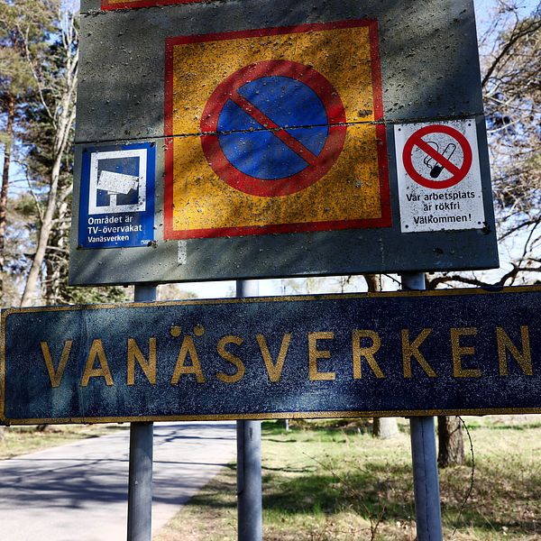 Skyltar vid en väg med information om Vanaesverken. Den övre skylten visar en röd cirkel med en diagonalt svart linje som indikerar förbud mot parkering. Intill finns en symbol för TV-övervakning och en skylt som betonar att området är övervakat och välkomnar besökare.