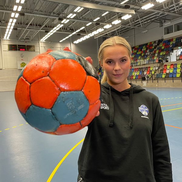 Handbollsspelare i sporthall håller en färgglad handboll mot kameran.