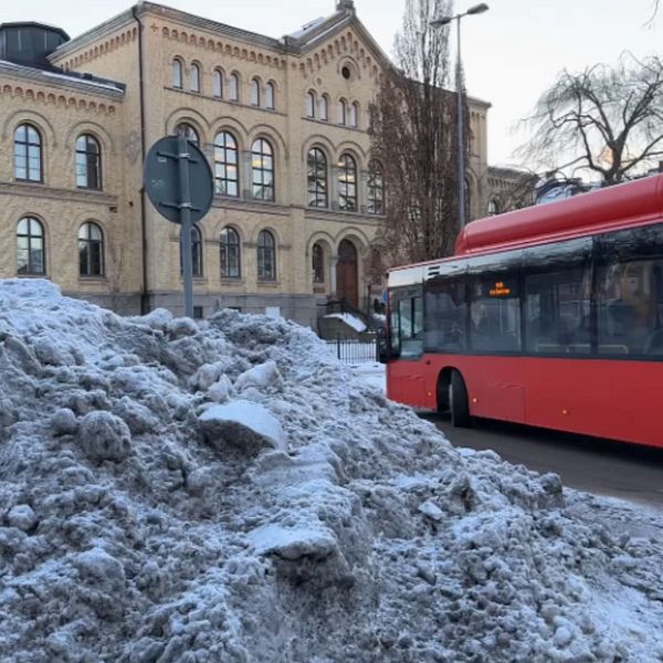 Röd buss som kör förbi snöhög.