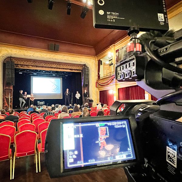En kamera dokumenterar ett möte som pågår i en teaterlokal.