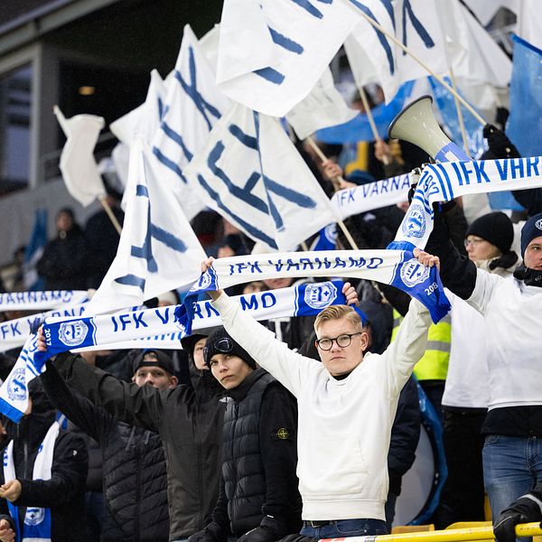 IFK Värnamo-fans viftar med flaggor och halsdukar på läktaren under en fotbollsmatch.