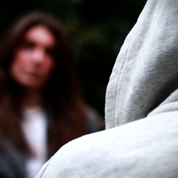 En person sitter med huvan uppdragen. I bakgrunden syns SVT:s reporter.