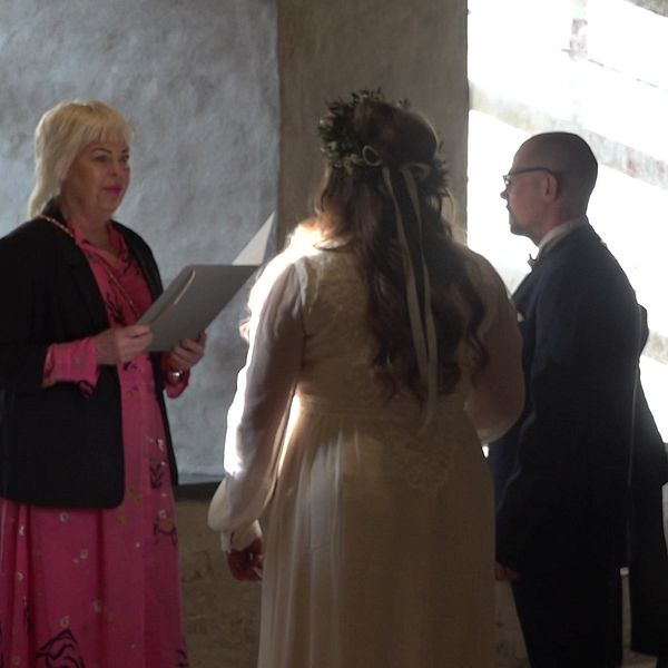 Brudpar samt vigselförrättare på Kalmar slott. Brudparet står framför ett fönster och solen skiner in.