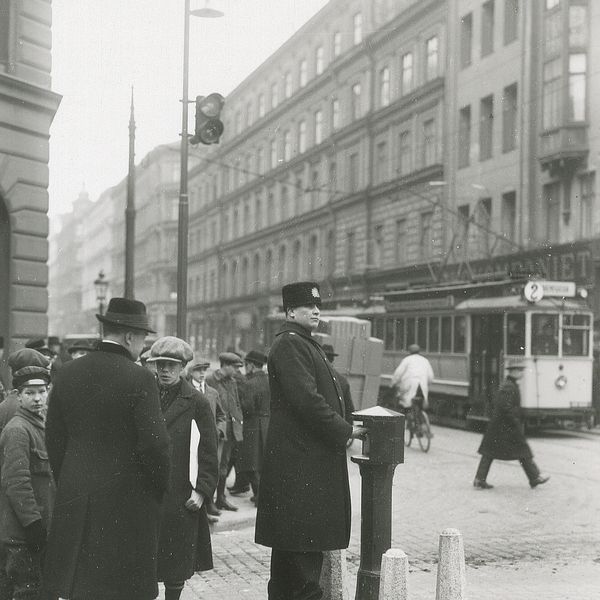 Svartvit gatubild med spårvagn och fotgängare i historisk stadsmiljö i Stockholm.