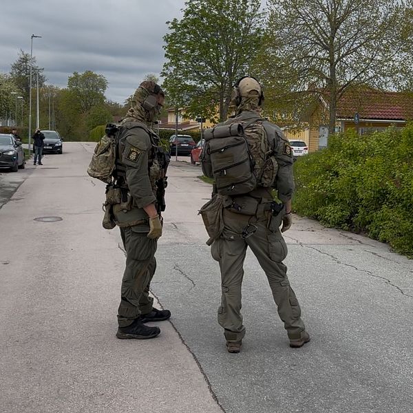 Två tungt beväpnade poliser står på en avspärrad gata i bostadsområde.